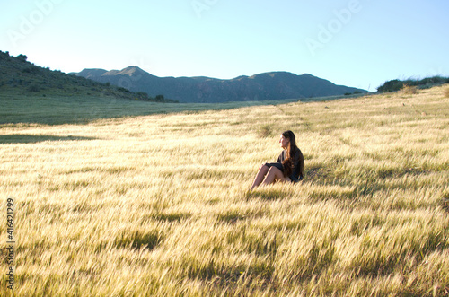 young woman sitting in a meadow illuminated by beautiful sunlight © javiemebravo