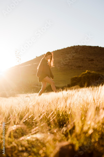 young woman walking through a meadow illuminated by beautiful sunlight
