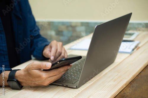 Hand using phone with laptop working at home