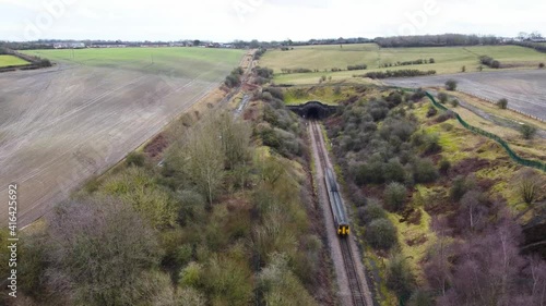 An aerial drone shot of a small 2 carriage passenger train travelling into a railway tunnel. photo