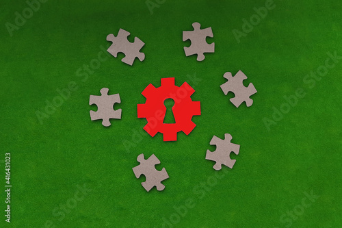 A gear with a keyhole in red, cardboard puzzles on a green background. Business project. Problem solving, approach.