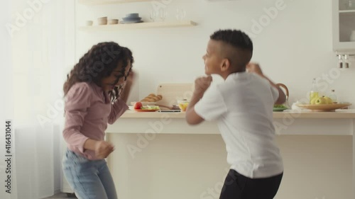 Happy black little brother and sister dancing together at kitchen, having fun and home photo