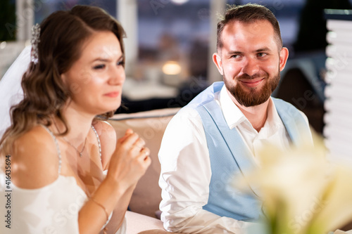newlyweds sit at table in restaurant and listen to congratulations from guests.