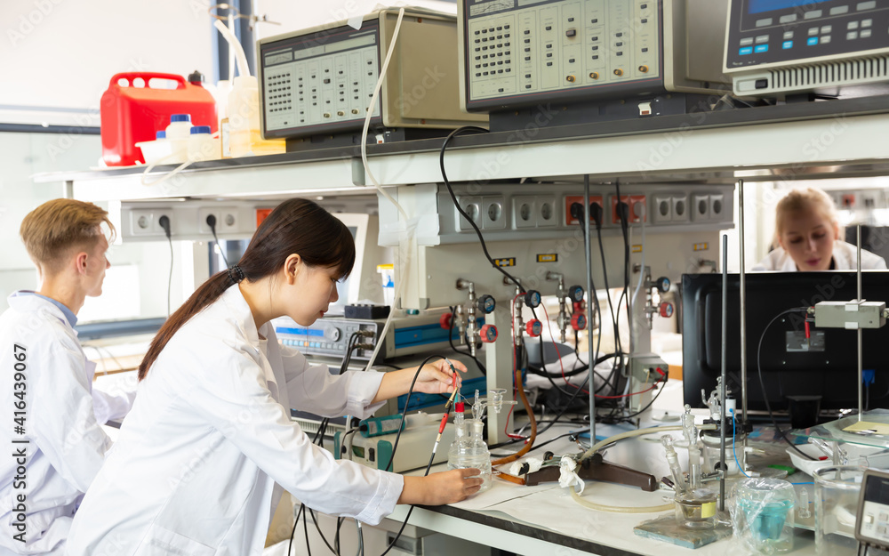 Positive Chinese female scientist near laboratory equipment at biochemical lab