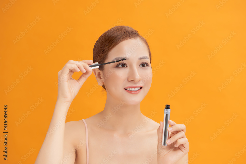 Obraz premium young beautiful woman Applying mascara isolated on yellow