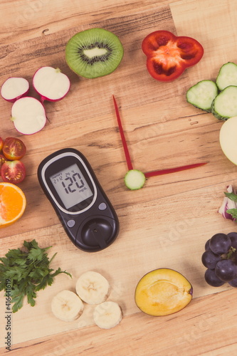 Glucometer with result of sugar level and clock made of fruits with vegetables