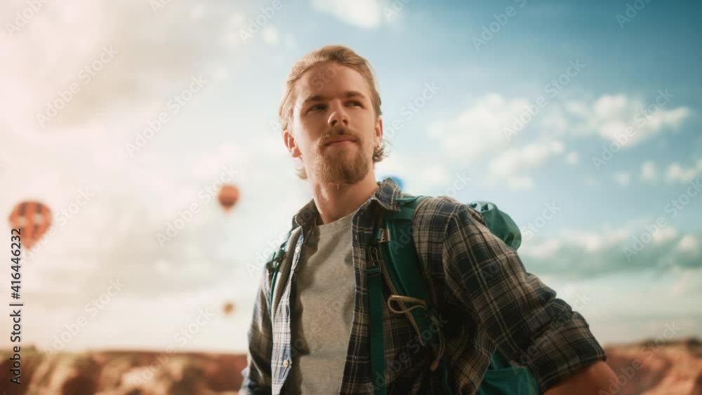 Portrait of a Young Handsome Tourist Posing with Backpack on Top of a Rocky Canyon Valley. Adventurous Male Backpacker on a Hiking Journey Trip. Hot Air Balloon Festival in Mountain National Park. Portrait of a Young Handsome Tourist Posing with Backpack on Top of a Rocky Canyon Valley. Adventurous Male Backpacker on a Hiking Journey Trip. Hot Air Balloon Festival in Mountain National Park.