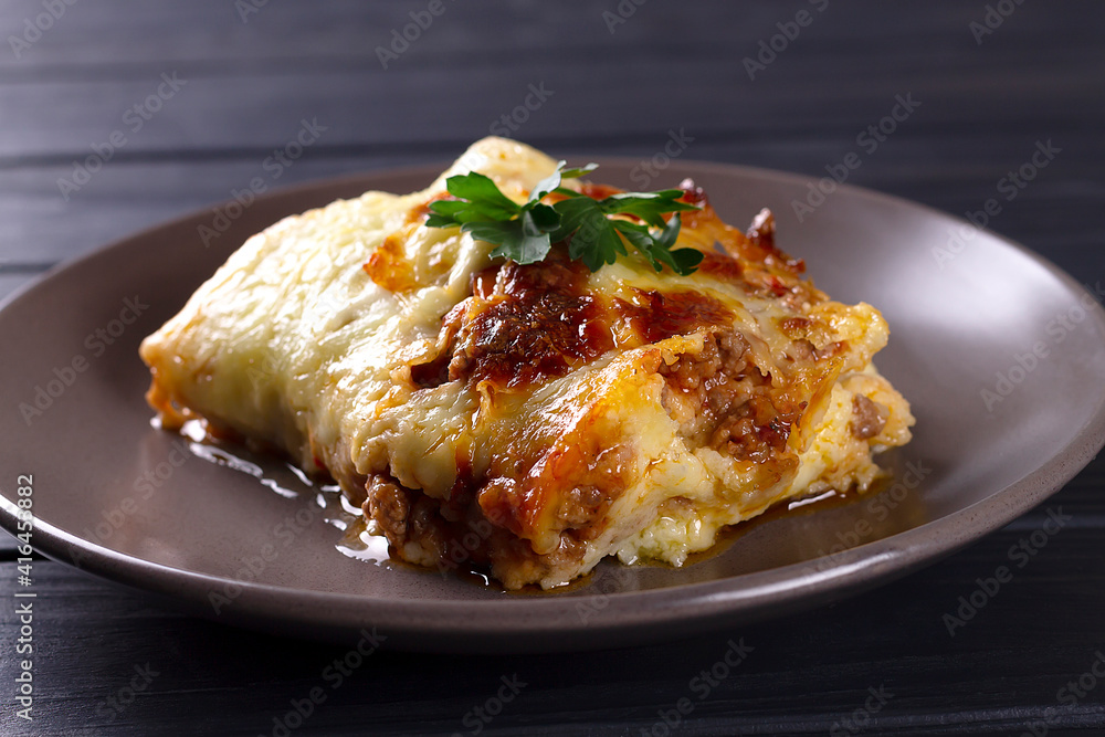 Italian lasagna with meat, cheese, herbs and tomato sauce, in a gray plate, on a wooden table.