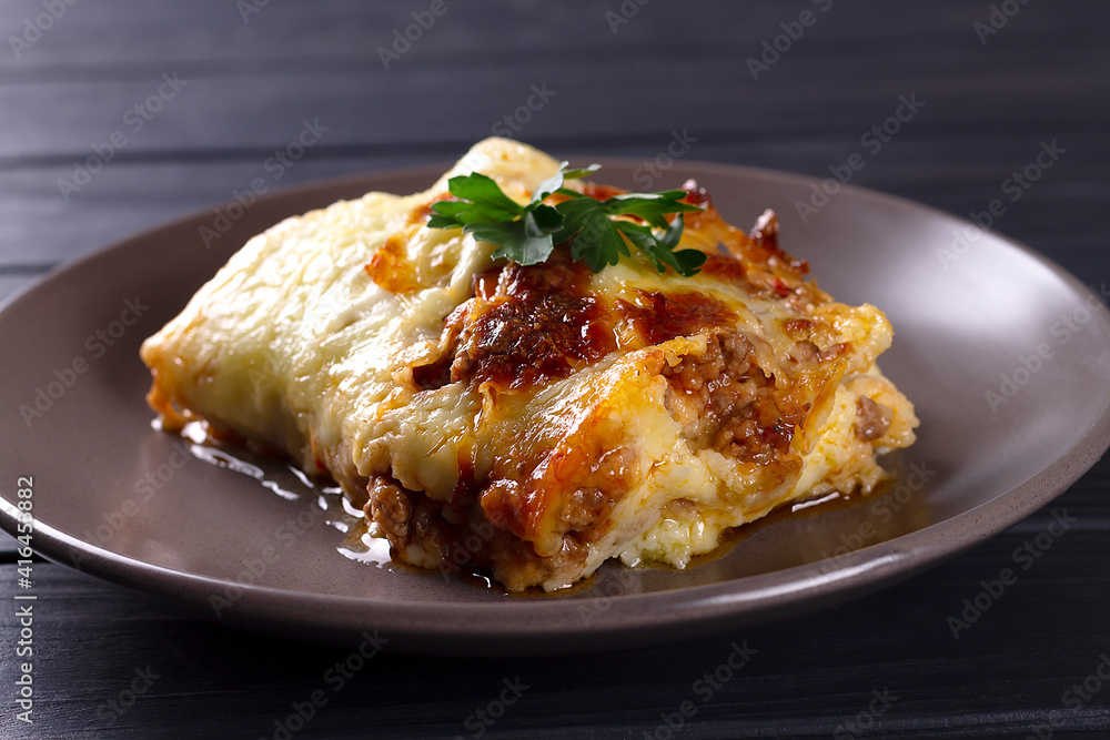 Italian lasagna with meat, cheese, herbs and tomato sauce, in a gray plate, on a wooden table. Italian lasagna with meat, cheese, herbs and tomato sauce, in a gray plate, on a wooden table.