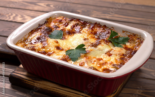 Italian lasagna with meat, cheese, herbs and tomato sauce, in a baking tray, on a wooden table.