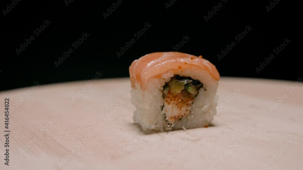 Piece of California roll sushi with salmon rotating on wooden board. Close up Piece of California roll sushi with salmon rotating on wooden board. Close up