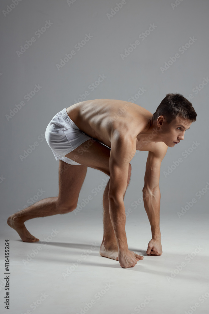 Obraz premium athlete with a pumped-up torso in white shorts on a gray background leaned forward 