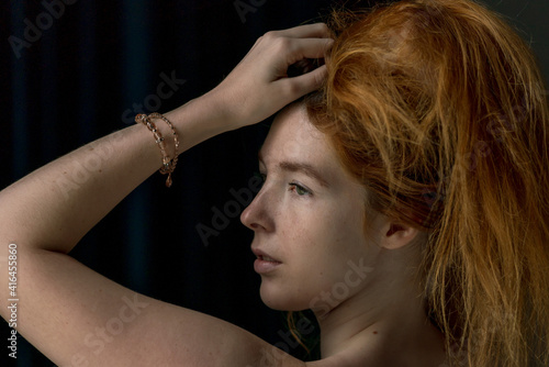 Face close up of Ginger hair young white model combing her hair upward with black background