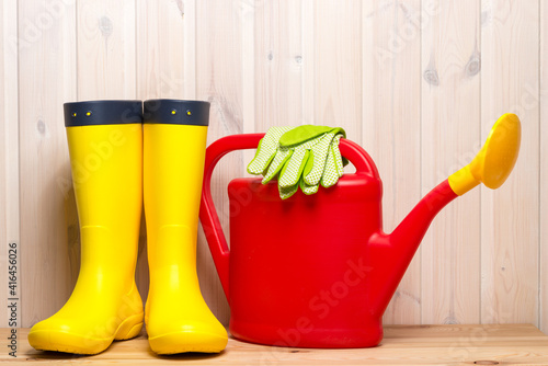 rubber boots, watering can and gardening gloves in spring objects on wooden background