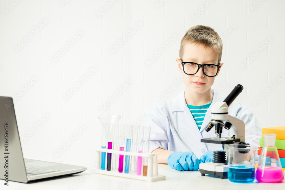 A schoolboy with a microscope examines chemicals in test tubes, conducts experiments - a portrait on a white background. Concept for the study of coronavirus in the laboratory