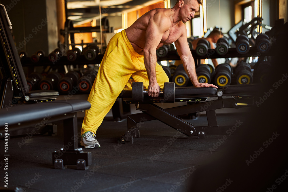 Obraz premium Serious body-builder using pair of dumbbells at gym