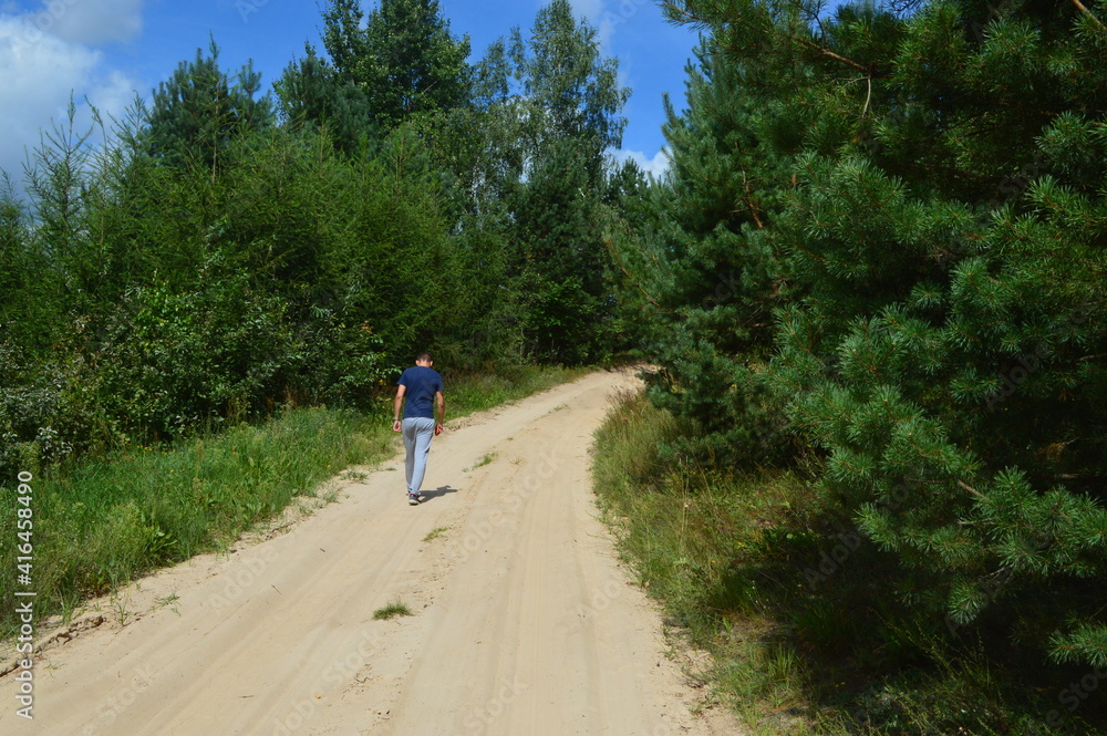Obraz premium A man walking along the rural road. A guy is in the nature. A foto of a walking guy. 