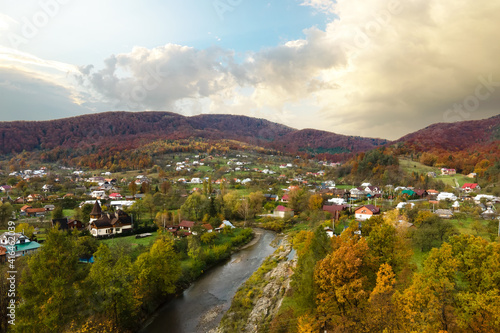 Foto Aerial view of a village rural area with small houses between autumn mountain hills covered with yellow and green spruce forest