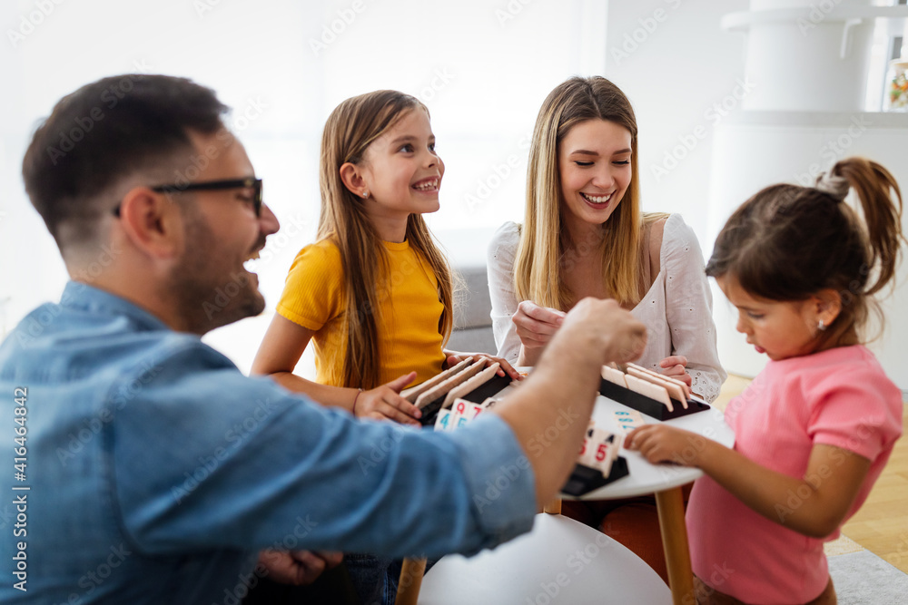 Obraz premium Happy young parents and children having fun, playing board game at home