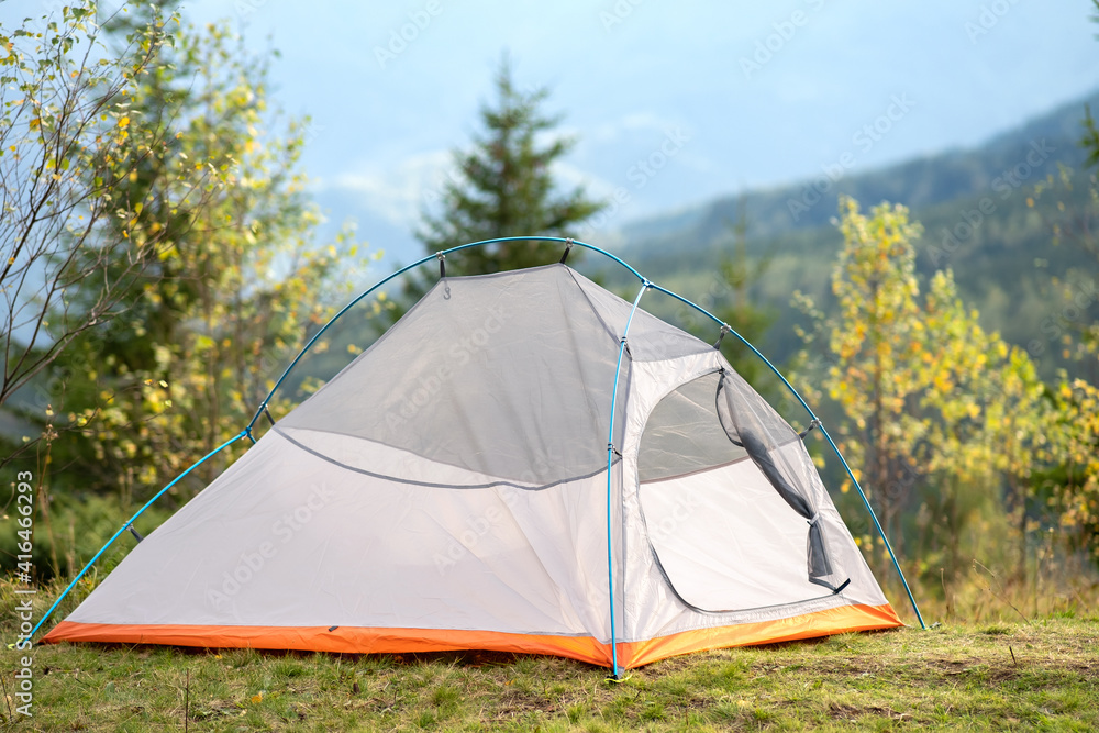 Empty camping tent standing on campsite with view of majestic high mountain peaks in distance. Hiking in wild nature and active trail travelling concept.