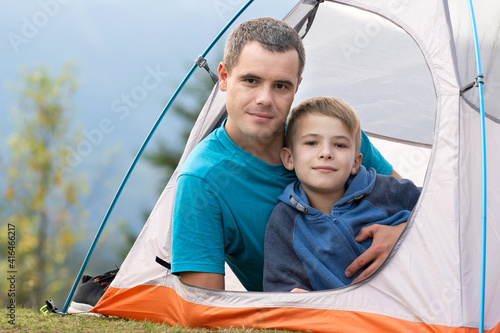 Young father with his child son resting together in a camping tent in summer mountains. Active family recreation concept.