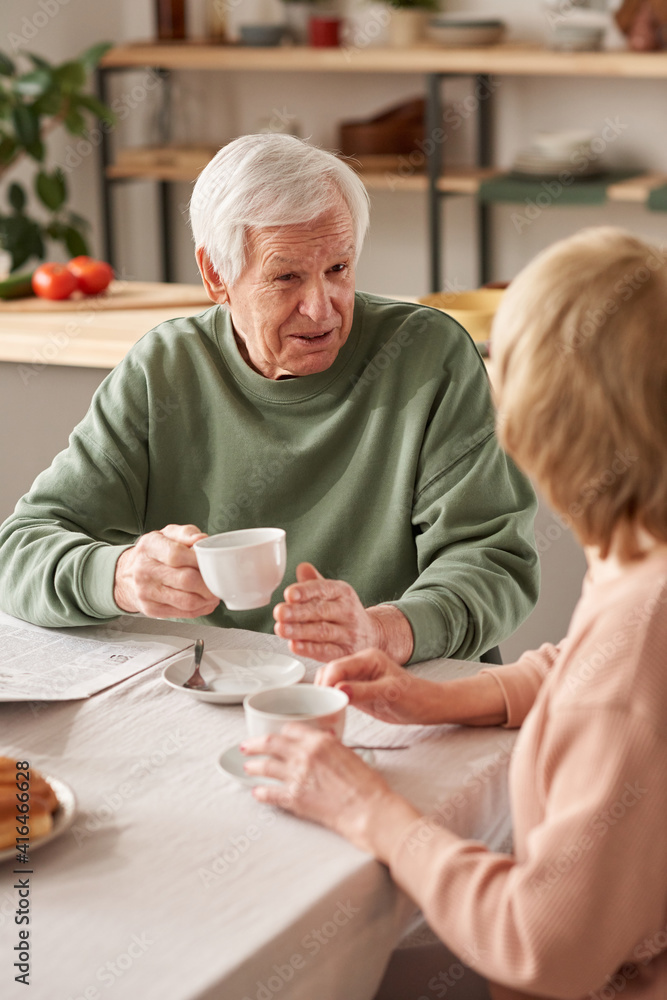 Senior man sitting at the table drinking tea together with his wife and talking in the kitchen Senior man sitting at the table drinking tea together with his wife and talking in the kitchen