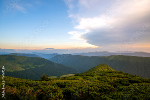 Summer evening mountain landscape with grassy hills and distant peaks at colorful sunset.