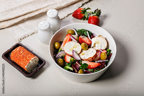 Delicious salad with fresh strawberries, red onions, ice salad, goat cheese and olives. Food still life on a light background. Organic farm products. Healthy food.