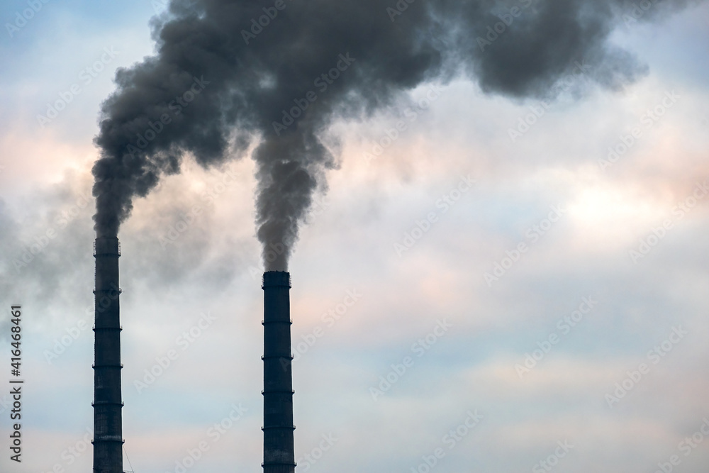 Coal power plant high pipes with black smoke moving up polluting atmosphere.