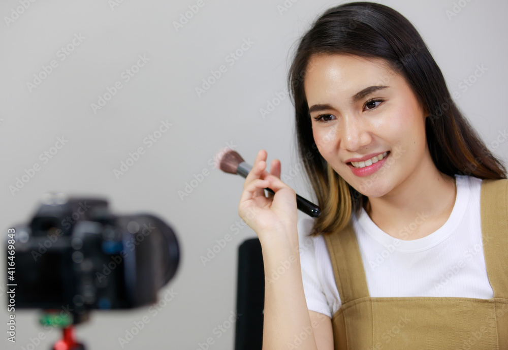 Smiling Asian young beauty blogger or Influencer show brushing make-up and recorded by using dslr camera. vlogger streaming online. Concept Selling products online. Smiling Asian young beauty blogger or Influencer show brushing make-up and recorded by using dslr camera. vlogger streaming online. Concept Selling products online.