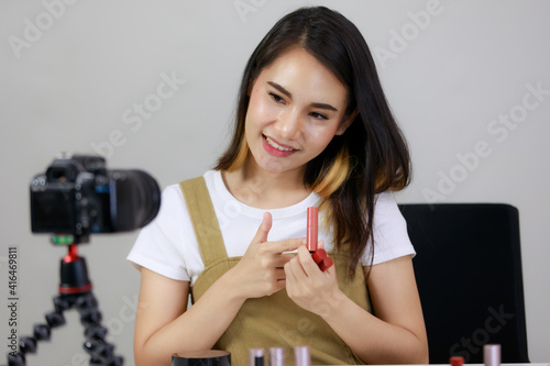 Smiling Asian young beauty blogger or Influencer show brushing make-up and recorded by using dslr camera. vlogger streaming online. Concept Selling products online.