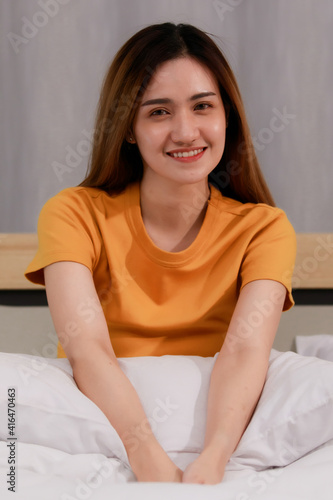 Image of Portrait smiling asian beautiful woman wearing a Orange dress hold pillow.Holding white pillows on the bed in the bedroom at home. Concept Smile woman cozy. © Bangkok Click Studio