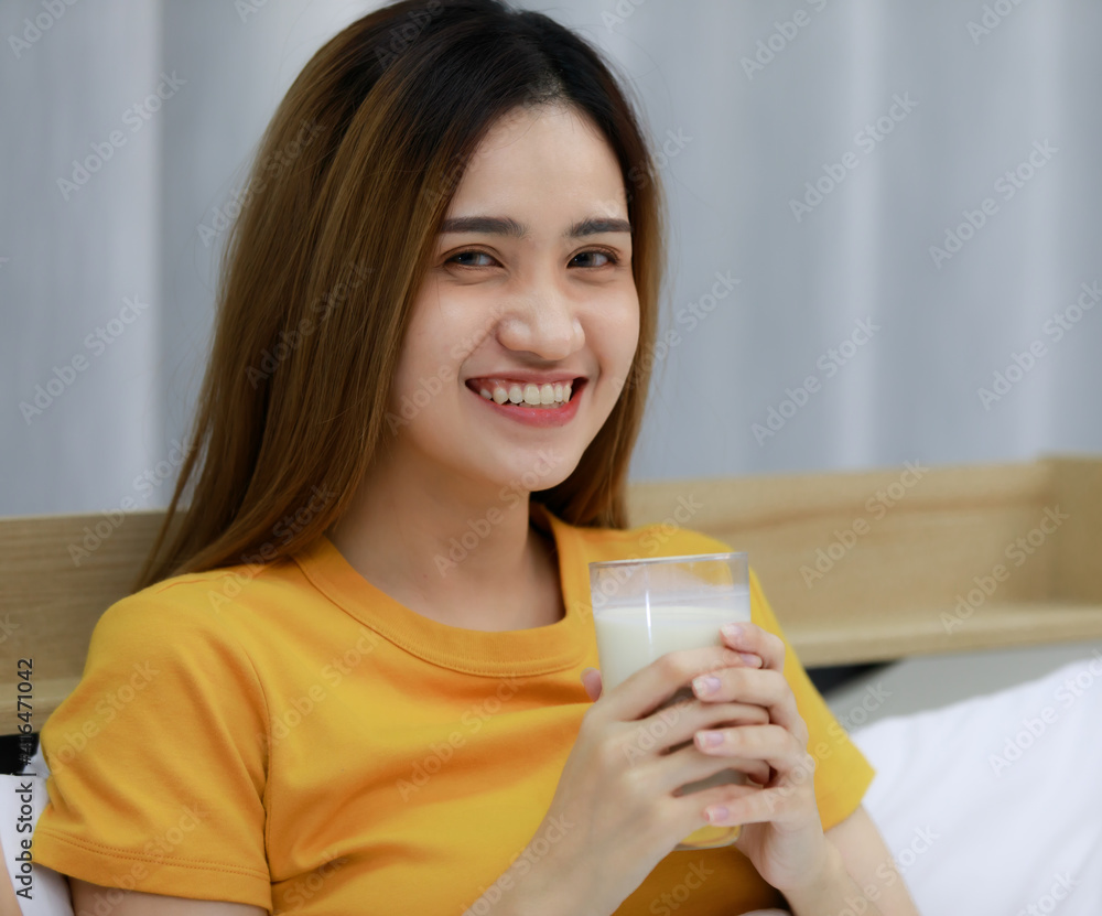 Smiling Asian young woman Looking at milk in the glass on white bed and happy in the bedroom at home. funny woman Before going to bed together on cozy. Concept Drink milk take care of health. Smiling Asian young woman Looking at milk in the glass on white bed and happy in the bedroom at home. funny woman Before going to bed together on cozy. Concept Drink milk take care of health.