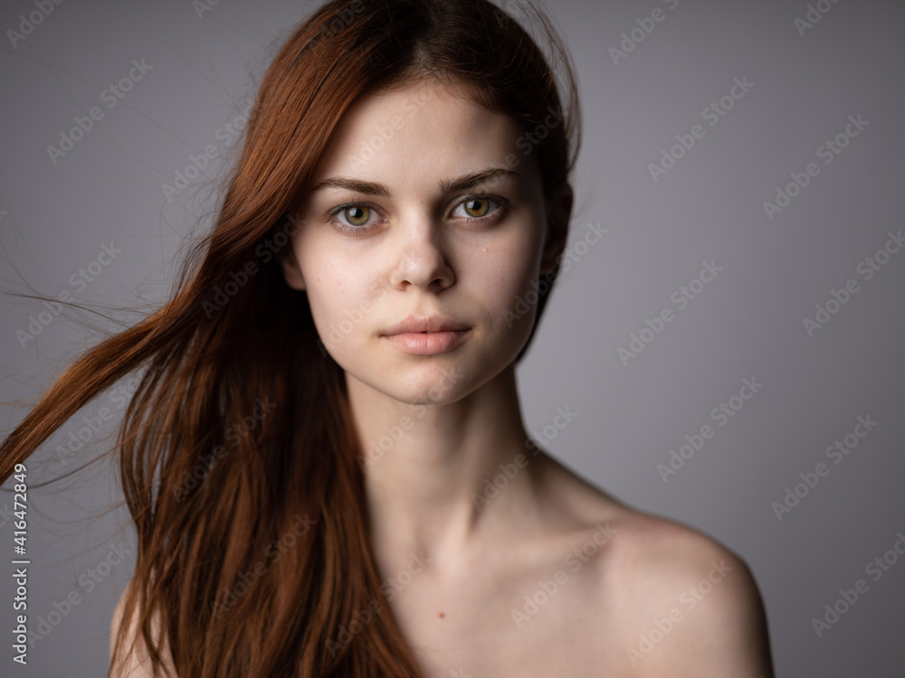 Portrait of a beautiful red-haired woman with bare shoulders on a gray background close-up Portrait of a beautiful red-haired woman with bare shoulders on a gray background close-up