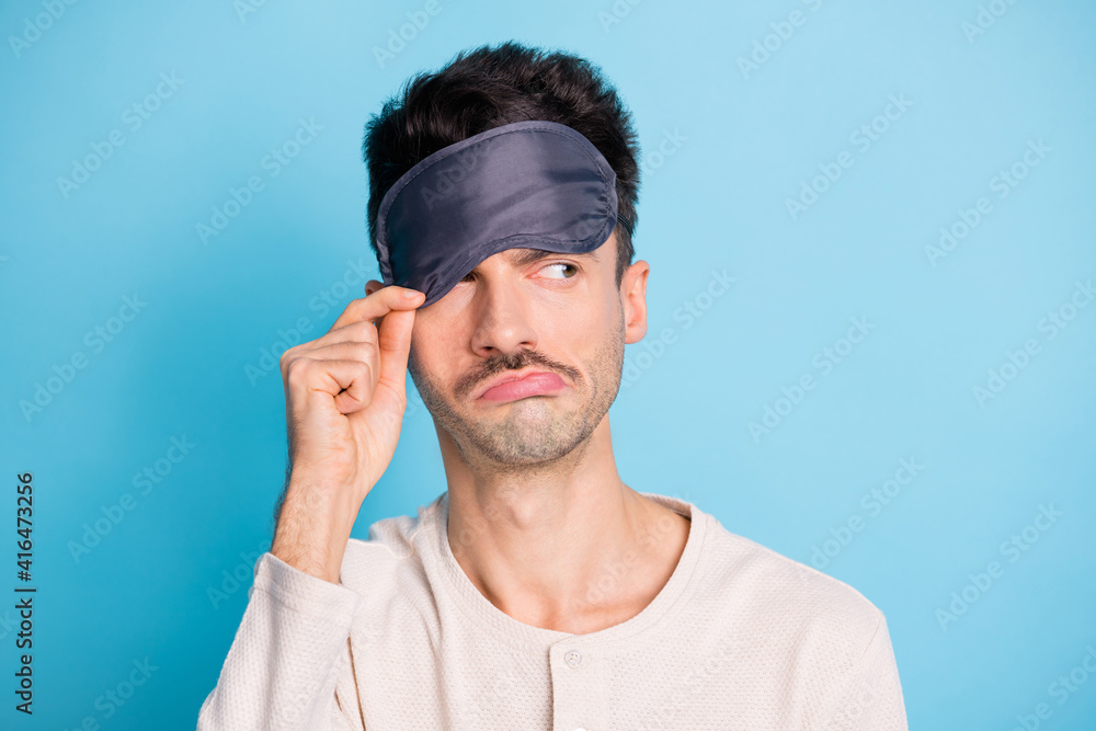 Portrait of lazy tired bored disappointed guy putting eye mask on looking aside isolated over bright blue color background Portrait of lazy tired bored disappointed guy putting eye mask on looking aside isolated over bright blue color background