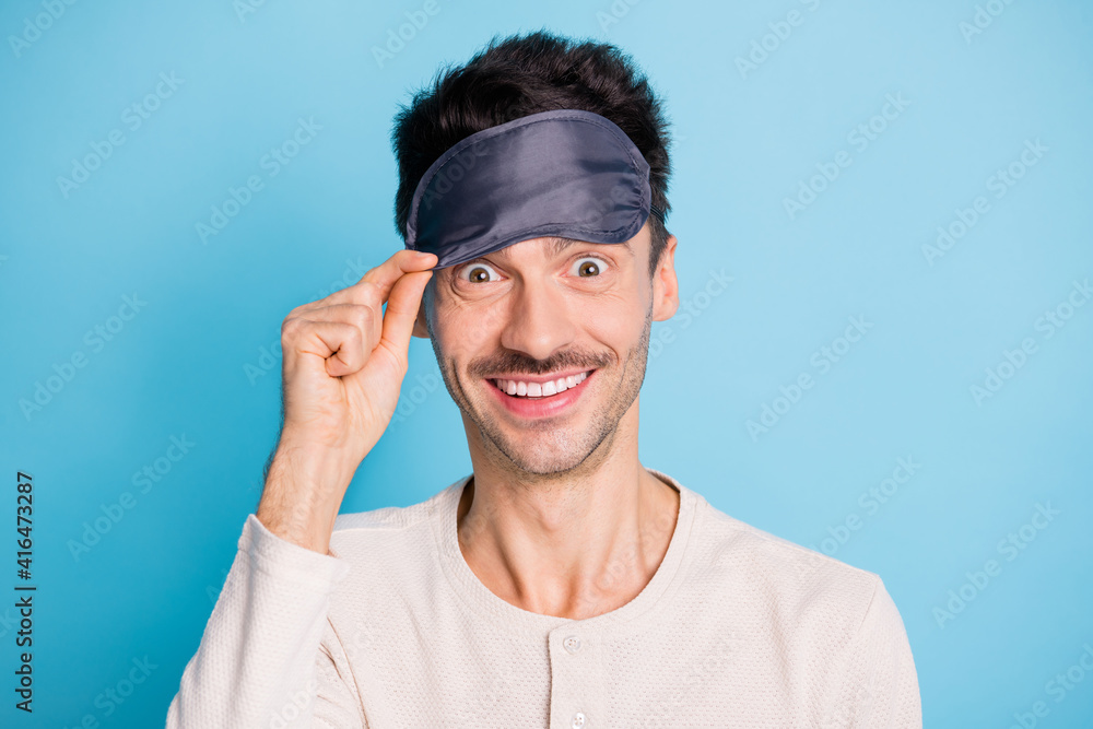 Portrait of nice cheerful funky brunet guy putting eye mask on having fun flight isolated over bright blue color background Portrait of nice cheerful funky brunet guy putting eye mask on having fun flight isolated over bright blue color background