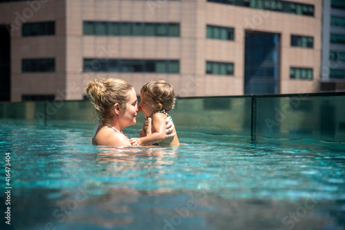 young mother swimng with her little toddler daughter in the pool on the roof of a skyscraper in a metropolis © Maria