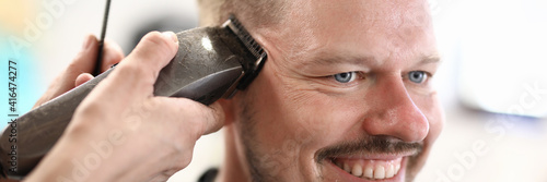 Portrait of smiling man whose master cuts with machine. Hairdressing services concept