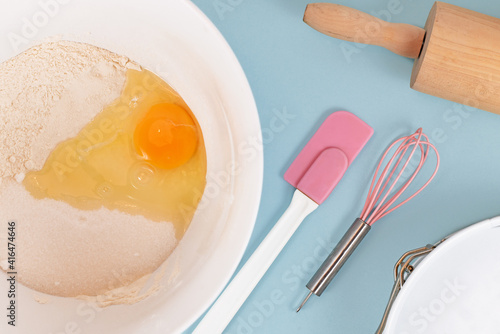 Preparing dough for shortcrust cake base with flour, sugar, baking bowder and egg in mixing bowl next to kitchen utensils photo