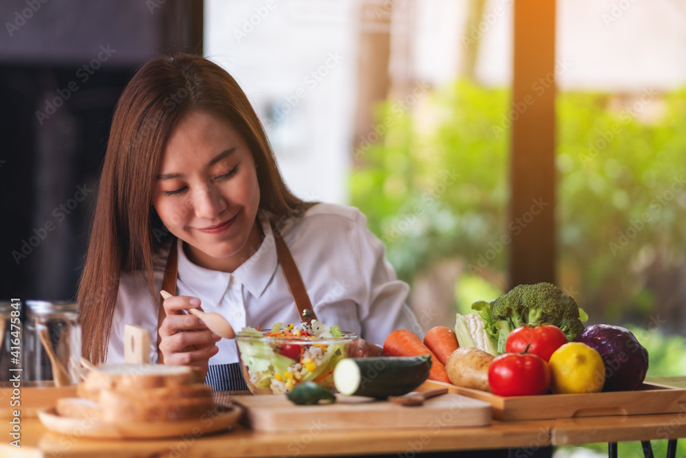 Closeup image of a beautiful young asian female chef cooking fresh mixed vegetables salad in kitchen
