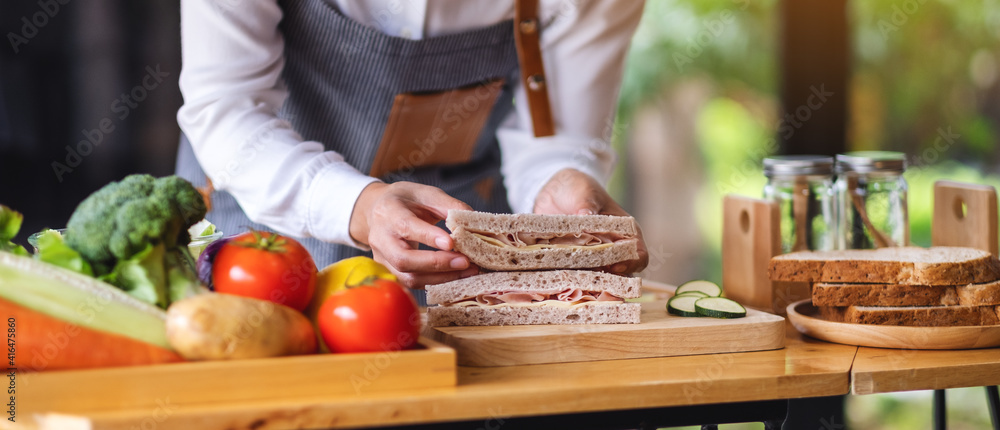 Closeup image of a female chef cooking and holding a piece of whole wheat ham cheese sandwich in kitchen