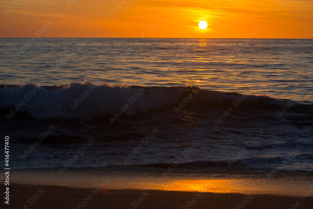 sunset on the ocean beach with big waves and orange sky 