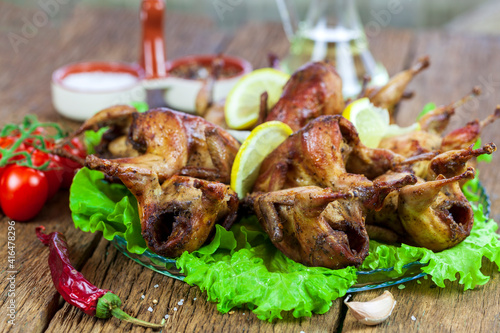 Barbecue fried quail carcasses with on orange with tomatoes and fresh parsley, on a wooden background