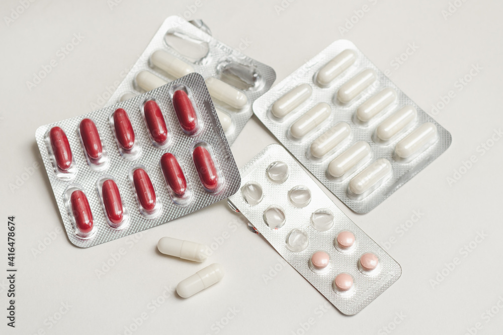 Capsules and tablets with medicine and vitamins in blisters and on a white surface, selective focus Capsules and tablets with medicine and vitamins in blisters and on a white surface, selective focus