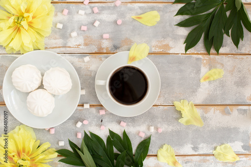 Morning coffee, marshmallows and beautiful yellow peony flowers on light table top view in flat lay style. Cozy breakfast on Mother or Woman day. photo