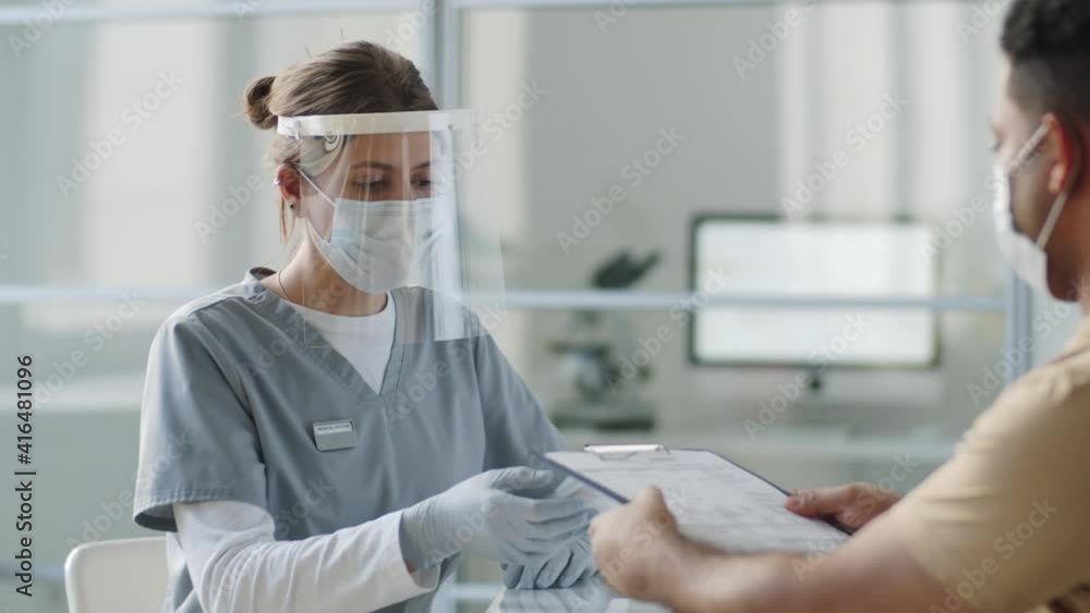 Female doctor in protective face shield, mask and gloves taking medical history and speaking with male patient while giving consultation during coronavirus outbreak Female doctor in protective face shield, mask and gloves taking medical history and speaking with male patient while giving consultation during coronavirus outbreak