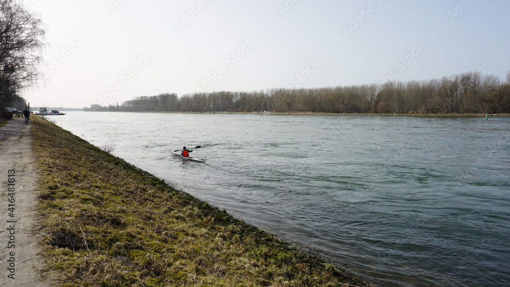a man in a kayak and the view of the ferry terminal in Neuburg am Rhein (Rheinland Pfalz on the right) and the ferry terminal in Neuburgweier (Baden-Wuerttemberg on the left) in Germany, in February