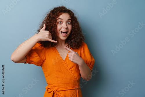 Happy redhead curly girl showing handset gesture and smiling
