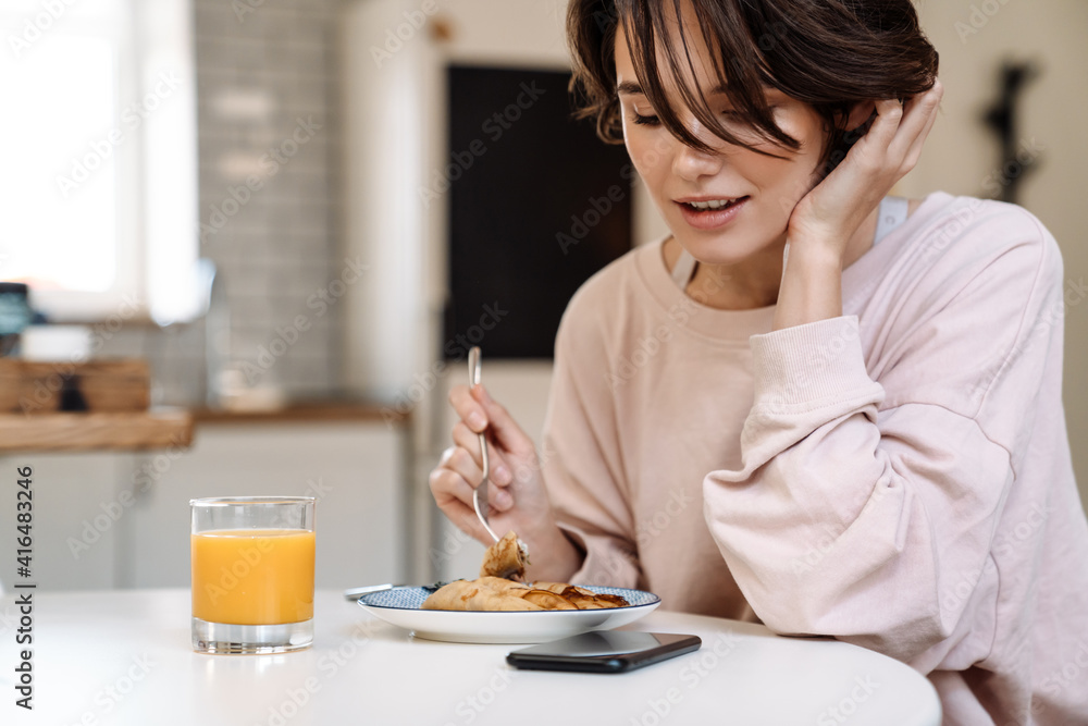 Pleased beautiful girl having breakfast while sitting at table Pleased beautiful girl having breakfast while sitting at table