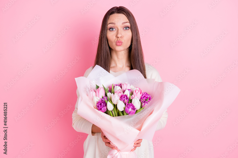 Portrait of gorgeous lady kiss lips arms hold flowers look camera isolated on pastel pink color background